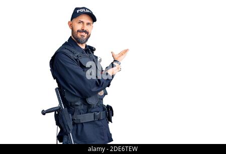 Junger, hübscher Mann in Polizeiuniform, der lächelnd zum Betreten einlädt Natur mit offener Hand Stockfoto