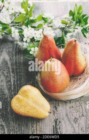 Korb aus Korbmetall, auf einem alten Holzhintergrund. Verschiedene Birnen, Pfirsiche und Trauben auf dem Tisch im Dorf. Stockfoto