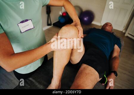 Weibliche Massage Therapeut Biegen Knie des verletzten Mannes liegend auf Sport-Massage-Bett im Rehabilitationsraum. Stockfoto