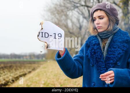 Frustriertes Mädchen mit Tränen bleiben auf freiem Feld und halten Papierbogen mit gedrucktem Text Covid-19, gegen Pandemie Welt Stockfoto