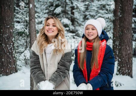 Nettes Teenager-Mädchen und ihre Mutter spielen mit Schnee während eines Winterspaziergangs im Wald. Stockfoto