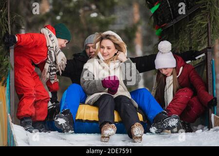 Mutter, Vater, Sohn und Tochter reiten im Winter von einer Eisrutsche auf einem mehrfarbigen Schlauch. Stockfoto