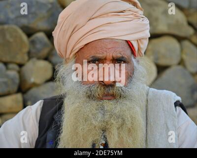 Ältere indische Hindu-Anhänger und Pilger mit dickem Vollbart und rosa Turban runzelten die Kamera während der Shivratri Mela (Bhavnath Fair) aus. Stockfoto