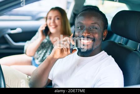 Junge interracial paar lächelnd glücklich im Gespräch auf dem Smartphone an das Auto. Stockfoto