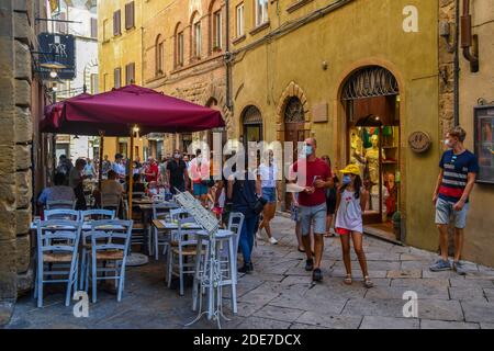 Ein Restaurant im Freien in einer engen Gasse der alten etruskischen Stadt Volterra mit Touristen im Sommer, Pisa, Toskana, Italien Stockfoto