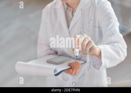 Nahaufnahme der unkenntlich Wissenschaftlerin Schreiben auf Glaswand und halten Zwischenablage während der Forschung im medizinischen Labor, kopieren Raum Stockfoto
