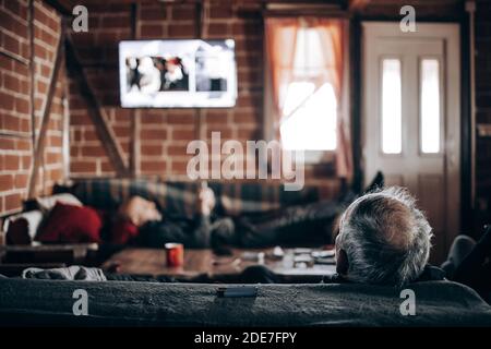 Älterer Mann, der Fernsehen schaut und auf einem Sofa sitzt. Rückansicht Stockfoto