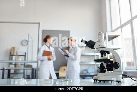 Portrait zweier Wissenschaftlerinnen, die im medizinischen Labor über Forschung diskutieren, Fokus auf Mikroskop im Vordergrund, Kopierraum Stockfoto