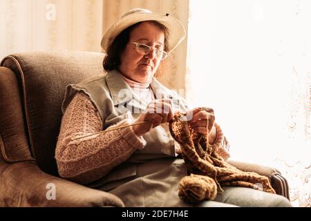 Ältere Frau strickt Pullover für ihre Enkel am Fenster Stockfoto