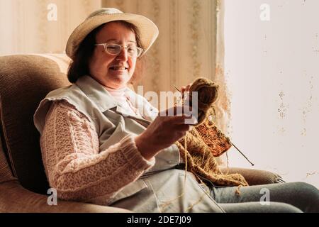 Ältere Frau strickt Pullover für ihre Enkel am Fenster Stockfoto