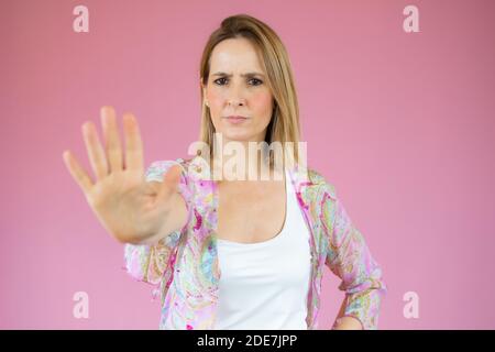 Porträt einer ernsthaften jungen Frau, die mit ausgestreckter Hand steht Zeigt Stoppgeste isoliert auf rosa Hintergrund Stockfoto