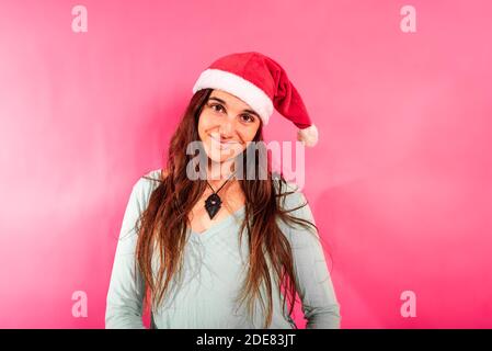 Hübsches junges Mädchen mit Sommersprossen und trägt Weihnachtsmann Hut, Blick auf Kamera entspannt und gelassen, isoliert auf femininen rosa Hintergrund und kopieren Raum. Stockfoto
