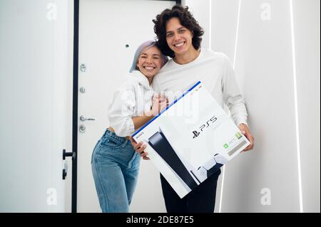 Ein glückliches junges Paar ist gerade mit einer brandneuen PlayStation 5-Spielekonsole von Sony aus dem Geschäft nach Hause gekommen. Sie haben es bei einem Black Friday-Verkauf bekommen. Moskau - November Stockfoto