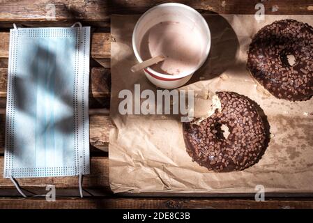 Essen im Freien: Donuts, ein Getränk in einem Einwegglas neben einer schützenden Gesichtsmaske. Eine Flatlay auf einer Bank in einem öffentlichen Park. Stockfoto