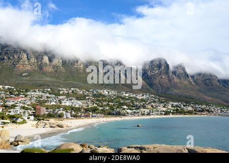 Glen Beach und Camps Bay Beach in Kapstadt, Südafrika mit zwölf Aposteln bedeckt von Wolken dahinter. Strand in Südafrika. Stockfoto