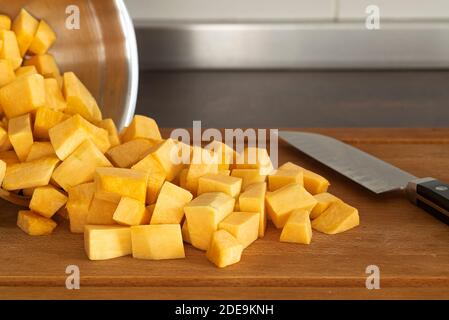 Schüssel mit Würfel Kürbis und Messer auf Holzbrett Stockfoto