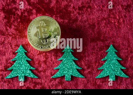 Stapel von Gold Bitcoins auf einem roten Samt Hintergrund, mit grünen Weihnachtsbäumen Stockfoto