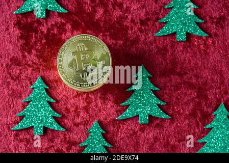 Stapel von Gold Bitcoins auf einem roten Samt Hintergrund, mit grünen Weihnachtsbäumen Stockfoto