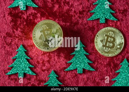 Stapel von Gold Bitcoins auf einem roten Samt Hintergrund, mit grünen Weihnachtsbäumen Stockfoto