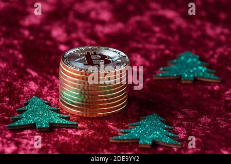 Stapel von Gold Bitcoins auf einem roten Samt Hintergrund, mit grünen Weihnachtsbäumen Stockfoto