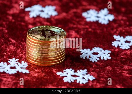 Stapel von Goldbitcoins auf einem roten Samthintergrund, mit weißen Schneeflocken Stockfoto