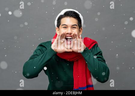 Aufgeregt junge asiatische Mann trägt Weihnachtskleidung schreien mit Händen Schröpfen um offenen Mund Stockfoto