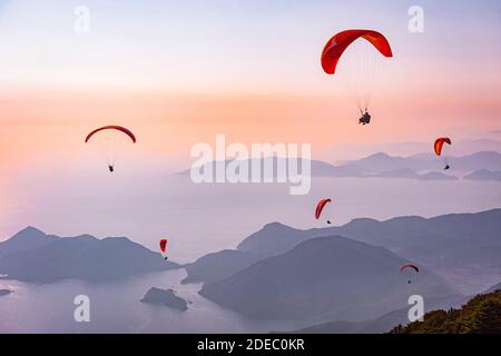Gleitschirmfliegen am Himmel. Gleitschirmfliegen Tandem über das Meer mit Bergen bei Sonnenuntergang. Luftaufnahme des Gleitschirms und der Blauen Lagune in Oludeniz, Mugla, Stockfoto