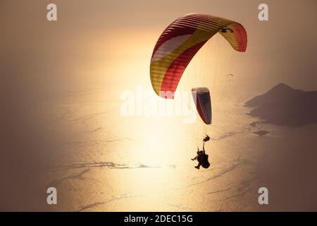 Gleitschirmfliegen am Himmel. Gleitschirmfliegen Tandem über das Meer mit Bergen bei Sonnenuntergang. Luftaufnahme des Gleitschirms und der Blauen Lagune in Oludeniz, Mugla, Stockfoto