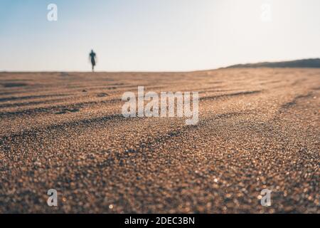 Silhouette Mann am Strand bei Sonnenuntergang zu Fuß. Nahaufnahme des welligen Sands. Sommer- und Reisekonzept. Stockfoto