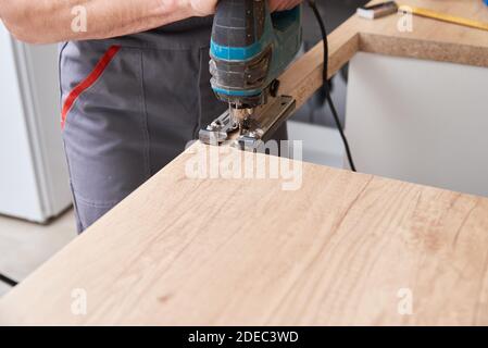 Reparaturman mit elektrischen Stichsäge. Sägeplatz für die Installation eines Gaskochfelds in einer Arbeitsplatte Stockfoto