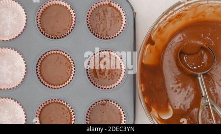 Mit einer Eislöffel Tortenklatsch in ausgekleidete Cupcake-Pfanne gießen. Schokolade Cupcakes mit Schokolade Zuckerguss Schritt für Schritt Rezept Stockfoto