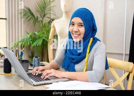 Asiatische muslimische Frau Designerin als Startup-Geschäft Inhaber arbeiten Mit Laptop-Computer in ihrem Schneidergeschäft Stockfoto