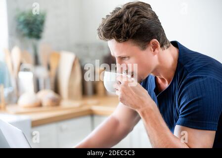 Zwangloser Mann, der morgens Kaffee trinkt, während er ernsthaft arbeitet Auf Laptop-Computer zu Hause Stockfoto