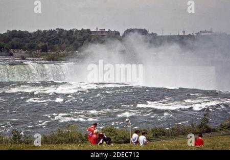 1970s Photo (1973) - Touristen im Park auf Goat Island Genießen Sie einen spektakulären Blick auf ''Horseshoe Falls;''' die kanadische Hälfte Der Niagarafälle Stockfoto