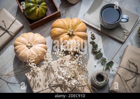Verpackte und bandagierte Geschenke, Kürbisse, eine Tasse Tee und getrocknete Pflanzen stehen auf dem Tisch. Vorbereitung auf den Geburtstag. Grunge Stockfoto