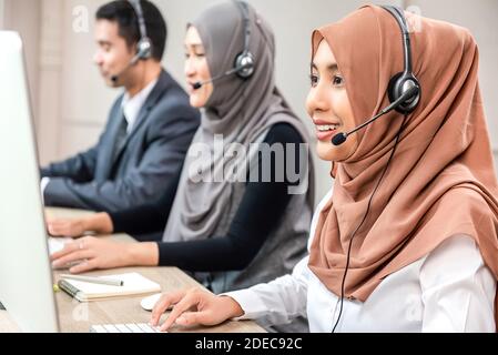 Freundliche schöne asiatische muslimische Frau trägt Mikrofon-Headset arbeiten als Kundendienstmitarbeiter mit Team im Callcenter Stockfoto