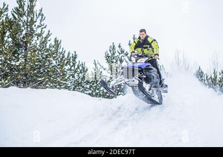 Springen auf einem Schneemobil auf einem Hintergrund des Winterwaldes. Helles Schneemobil. Sportler auf einem Schneemobil bewegen sich im Winterwald in den Bergen. Mann Stockfoto