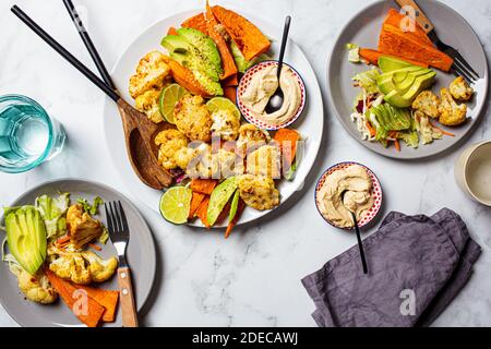 Veganes Lebensmittelkonzept. Gebackenes Gemüse mit Hummus in einer weißen Schale, weißer Marmorhintergrund. Stockfoto