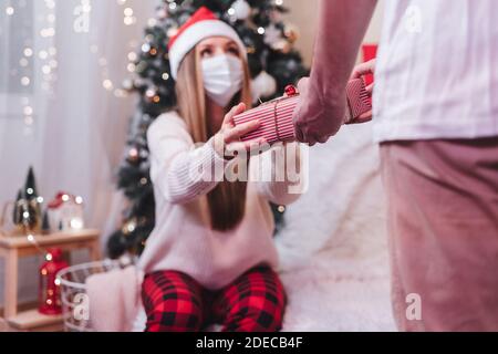 Romantisches Paar, das Geschenke austauscht. Frau in medizinischer Schutzmaske zu Weihnachten. Nahaufnahme Rückansicht des Mannes, der die gegenwärtige Kiste hinter seinem Rücken hält, während s Stockfoto
