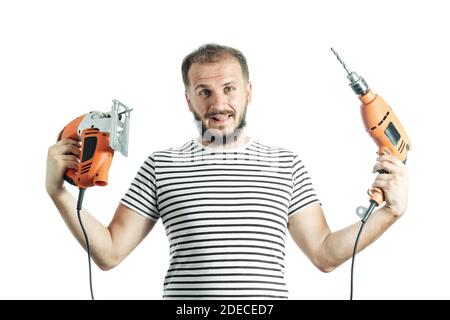 Ein dummer Mann hält einen Bohrer und ein elektrisches Puzzle in den Händen. So wählen Sie ein Elektrowerkzeug aus Stockfoto