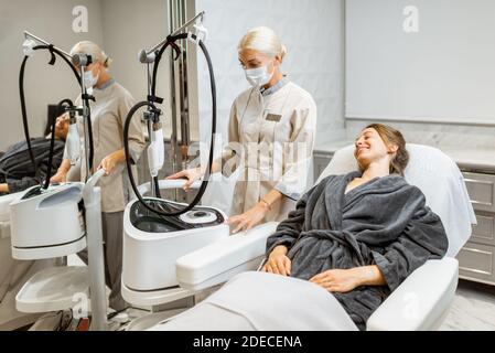 Junge Frau Client mit einem Arzt während einer Gesichtsverjüngung Behandlung im medizinischen SPA-Büro. Arzt in Gesichtsmaske. Konzept eines Unternehmens während einer Pandemie Stockfoto