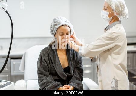 Junge Frau, die sich auf eine Verjüngungskur vorbereitet, trägt Schutzhut im medizinischen SPA-Büro mit einem Arzt Stockfoto