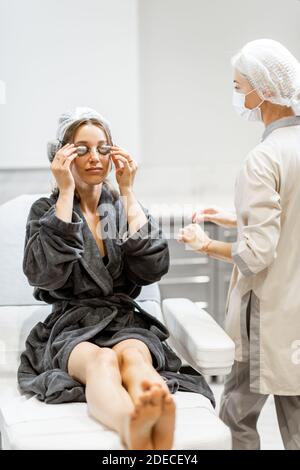 Junge Frau, die sich auf eine Verjüngungskur vorbereitet, trägt eine Schutzbrille im medizinischen SPA-Büro mit einem Arzt im Hintergrund Stockfoto