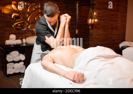Professioneller Masseur, der eine Tiefenmassage für einen männlichen Klienten im Spa Salon macht, Schultermassage Stockfoto
