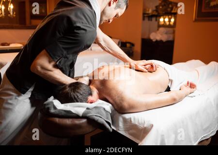 Professioneller Masseur, der eine tiefe Rückenmassage für einen Mann macht Kunde im Spa Salon Stockfoto