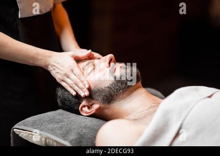 Bärtiger Mann, der eine Gesichtsmassage erhält, sich im Spa-Salon entspannt, Nahaufnahme Stockfoto