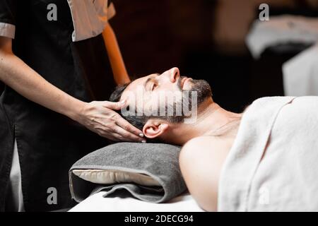 Bärtiger Mann, der eine Gesichtsmassage erhält, sich im Spa-Salon entspannt, Nahaufnahme Stockfoto