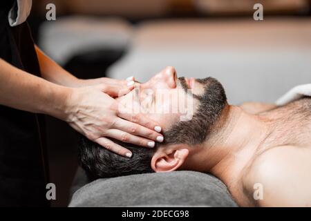 Bärtiger Mann, der eine Gesichtsmassage erhält, sich im Spa-Salon entspannt, Nahaufnahme Stockfoto