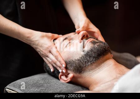 Bärtiger Mann, der eine Gesichtsmassage erhält, sich im Spa-Salon entspannt, Nahaufnahme Stockfoto