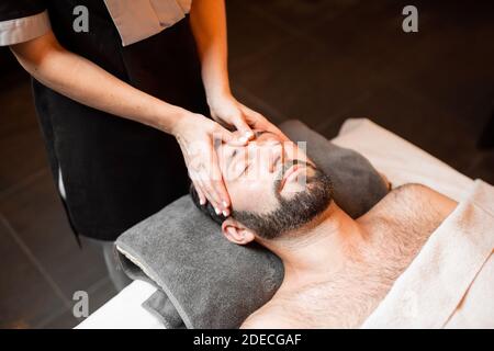 Bärtiger Mann, der eine Gesichtsmassage erhält, sich im Spa-Salon entspannt, Nahaufnahme Stockfoto